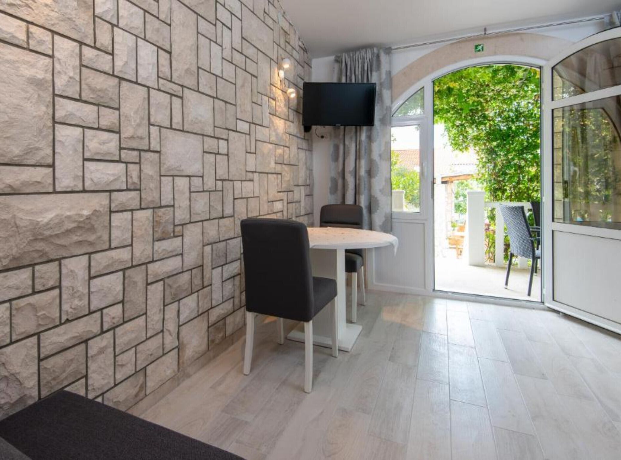 A room with a stone wall, a flat-screen TV mounted above a table with two chairs, and a large glass door leading outside.