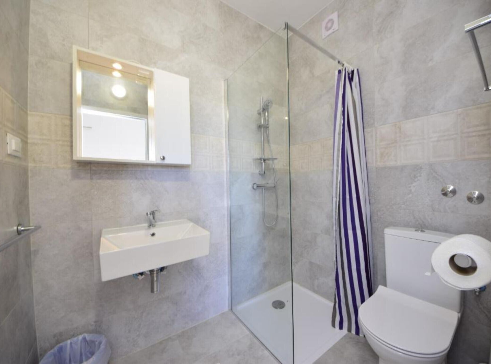A modern bathroom with a glass shower enclosure, a white sink, and a toilet.