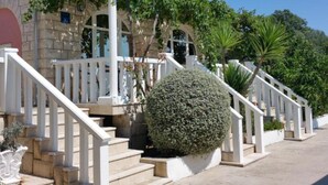A building with a stone facade, white railings, and a large spherical hedge. - Adriatic Guesthouse Balota with Shared Pool- Bungalow with Terrace (1) (Viganj)