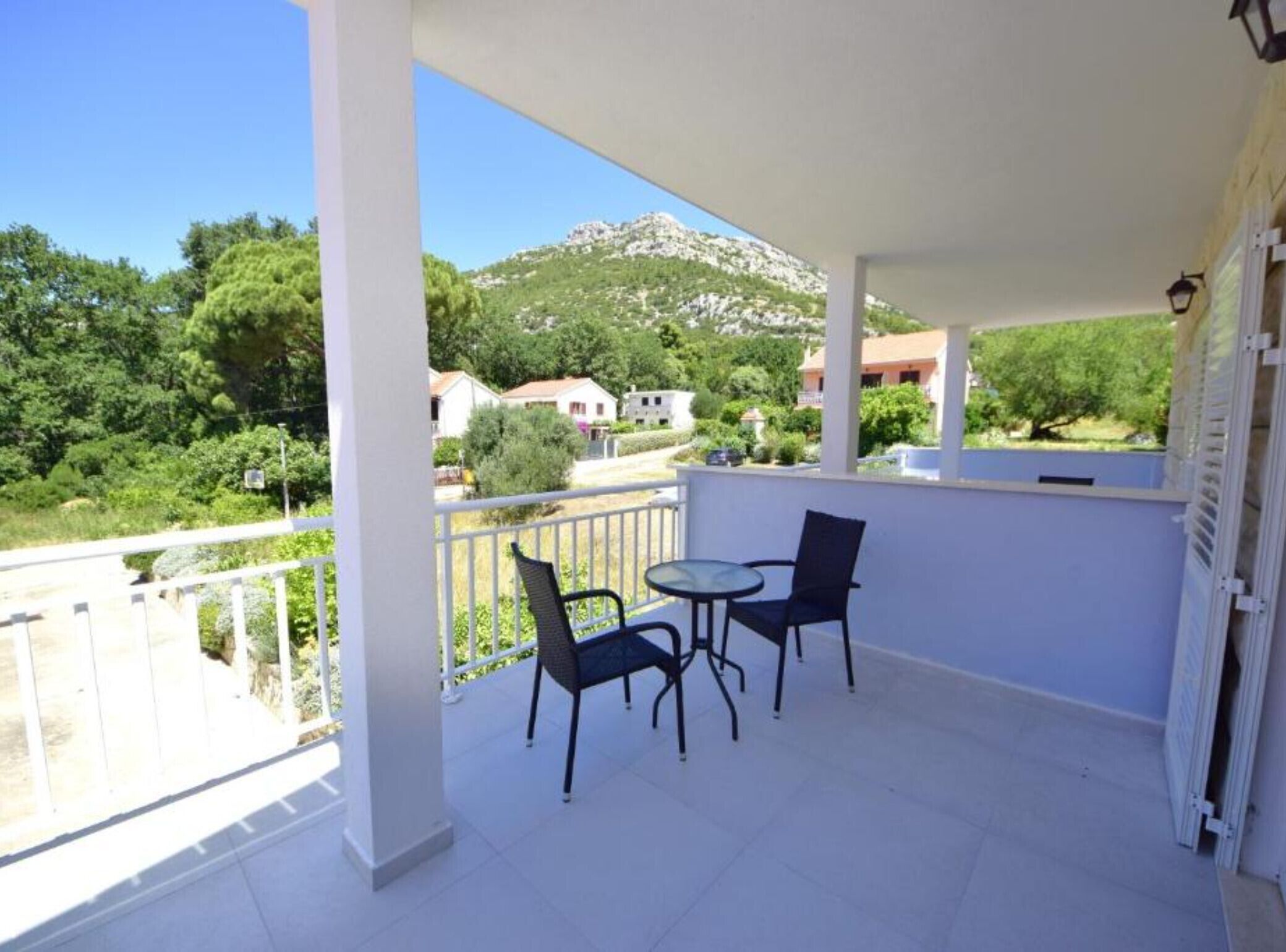 A balcony with two chairs and a table, overlooking a mountainous landscape with houses.