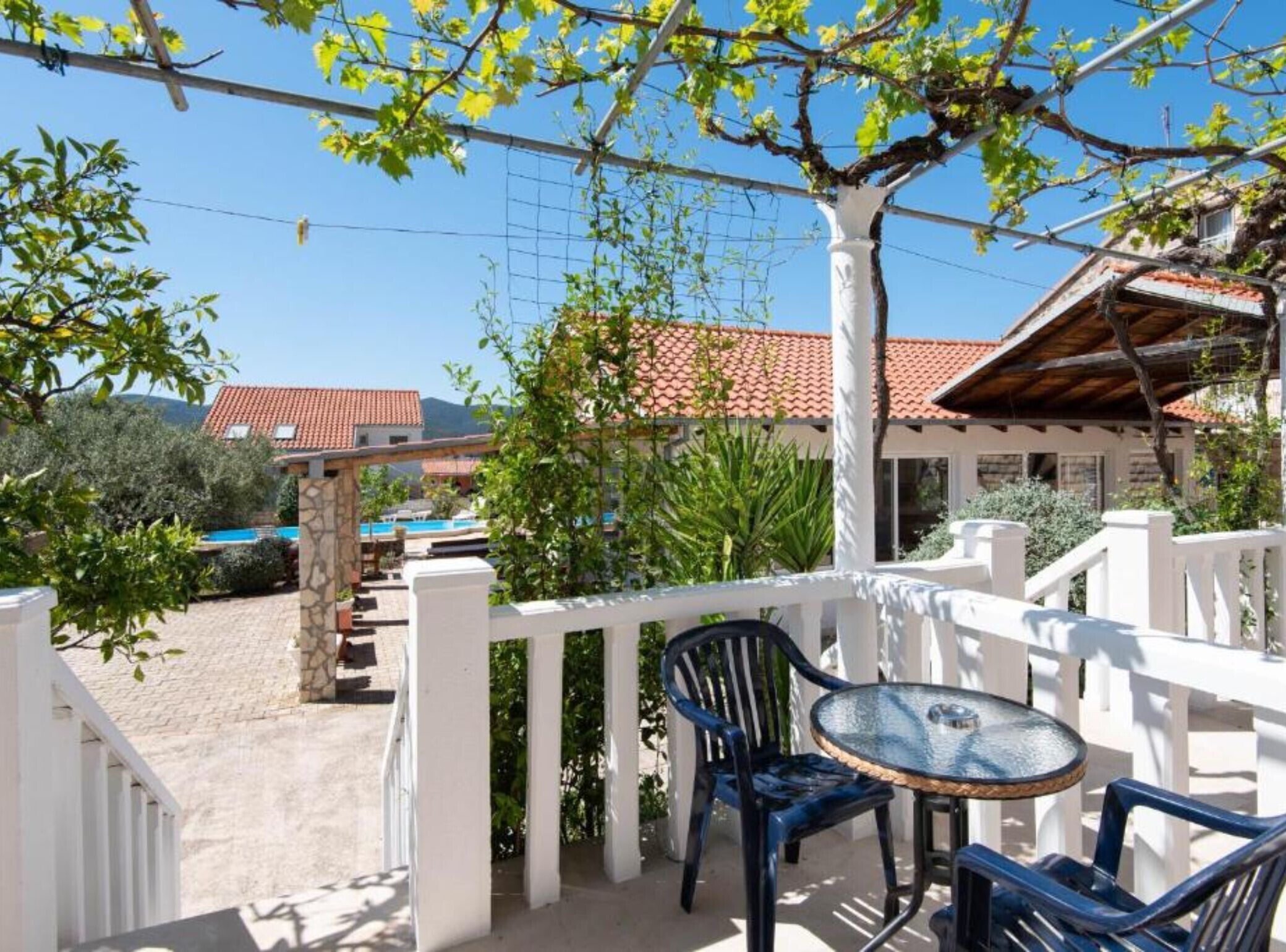 A balcony with a table and chairs, a white fence, and a view of a building with a red-tiled roof.