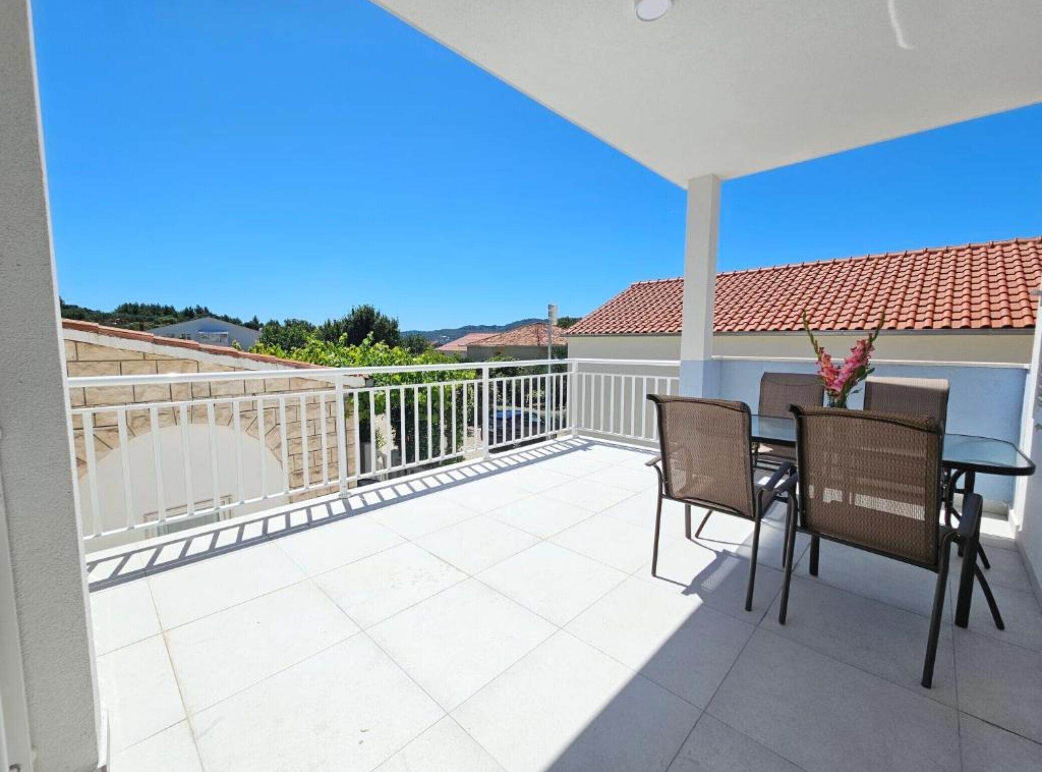 Un balcon avec une balustrade blanche, une table avec des chaises et une vue sur des immeubles et de la verdure.