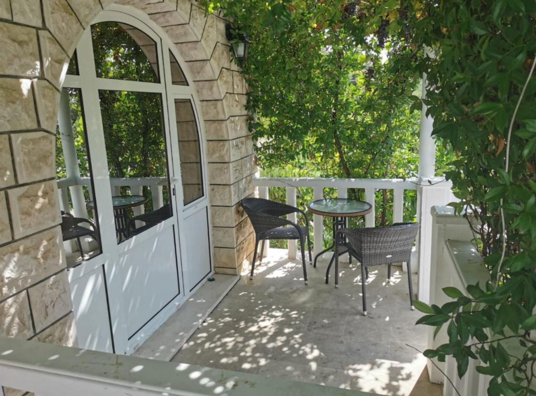 A covered patio with stone walls, a white railing, and outdoor furniture.