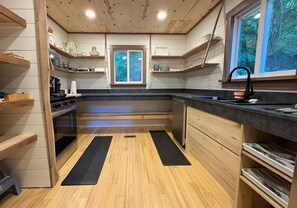 A modern kitchen with wooden cabinets, a black countertop, and a window with a view of greenery. - Ski-In ⛷ & Golf with Million-Dollar Mountain Views, Quick Drive to Asheville (Mars Hill)