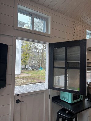 A room with a door leading to a backyard, a window with blinds, and a teal-colored appliance on a black countertop.
