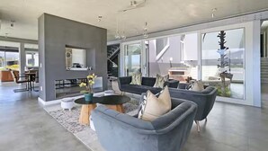 En rummelig opholdsstue med en grå sofasæt, et sofabord og et spiseområde med et køkken i baggrunden.