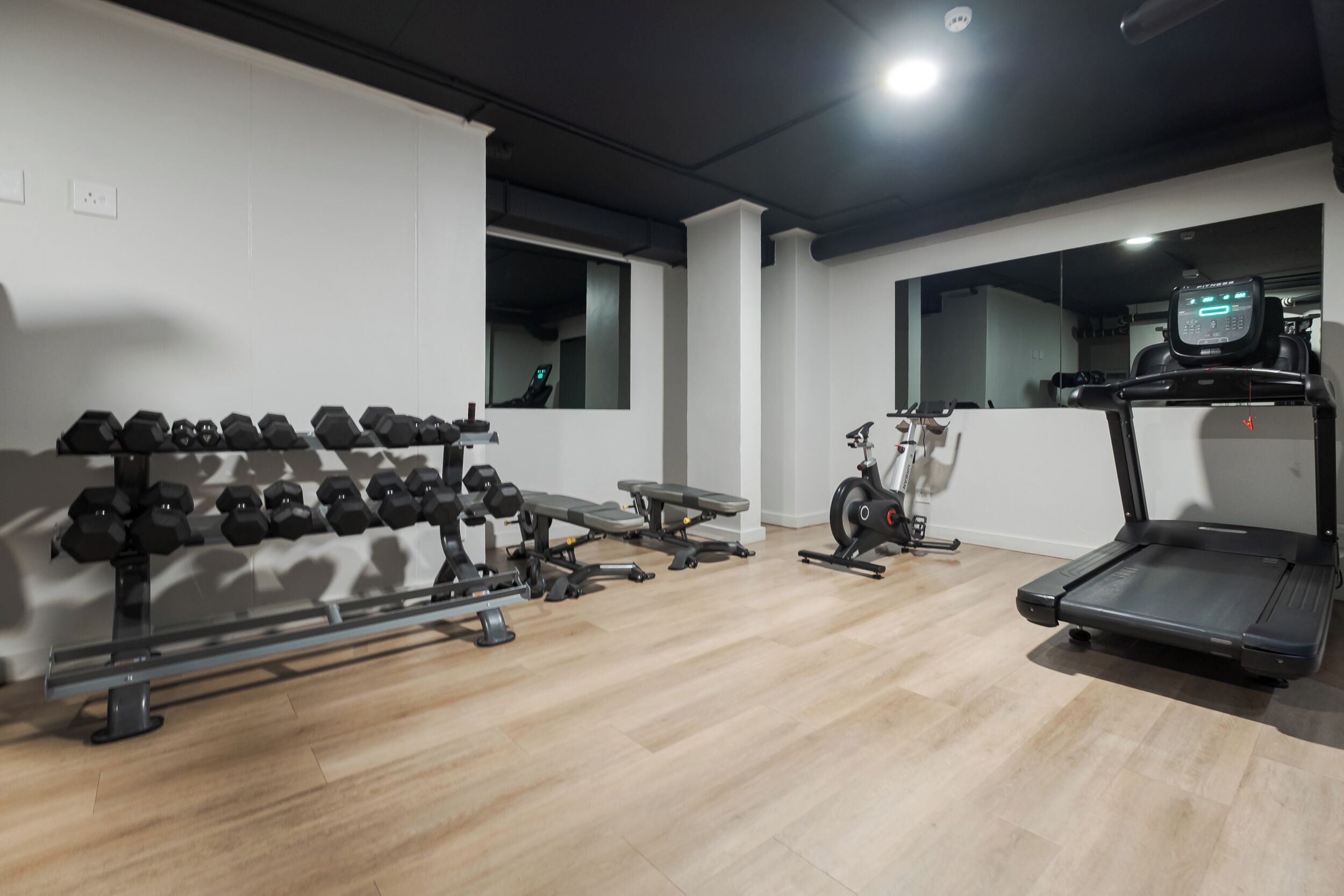 Une salle de sport équipée d’haltères, d’un banc, d’un vélo d’appartement et d’un tapis de course.