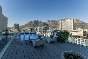 A rooftop pool with lounge chairs, a glass railing, and a view of a cityscape with mountains in the background. - 1205 at the Tokyo (Cape Town)