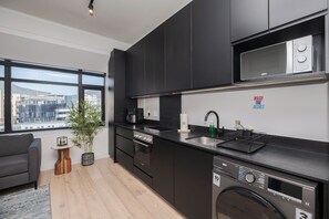A modern kitchen with black cabinets, a microwave, a dishwasher, and a large window offering a city view. - 1205 at the Tokyo (Cape Town)