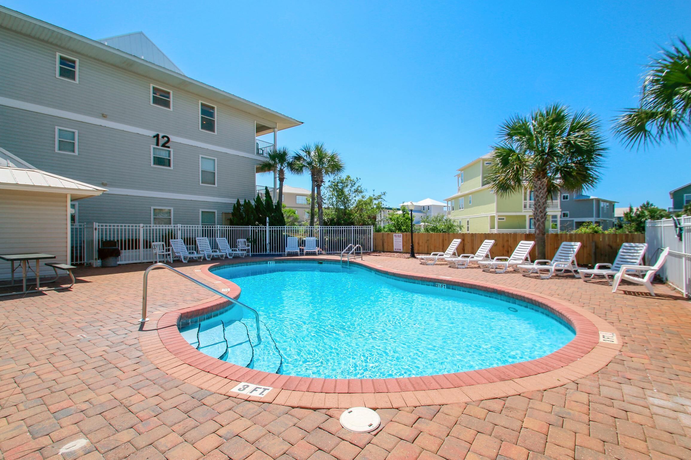 A rectangular swimming pool with a brick border, surrounded by lounge chairs and a fence.