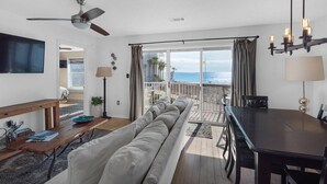 Una habitación con sofá, mesa de comedor, ventilador de techo y vista al océano.