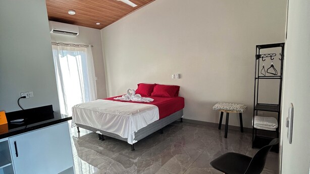 Une chambre moderne avec un lit, un ventilateur de plafond, un petit tabouret et une chaise.