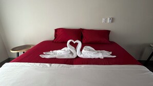 Un lit recouvert d’une couverture rouge, avec deux serviettes blanches disposées en forme de cœur.