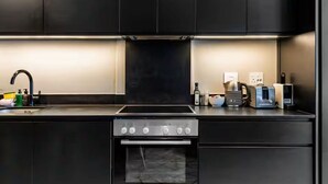 Une cuisine moderne avec des meubles de couleur sombre, un four encastré, une plaque de cuisson et divers appareils électroménagers posés sur le plan de travail.