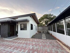 Una casa moderna con entrada pavimentada, porche cubierto y jardín cercado.
