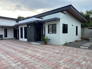 A modern two-story house with a paved driveway, large windows, and a small garden area.