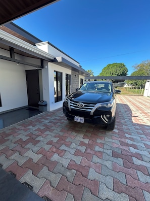 A modern building with a paved driveway and a black SUV parked in front.