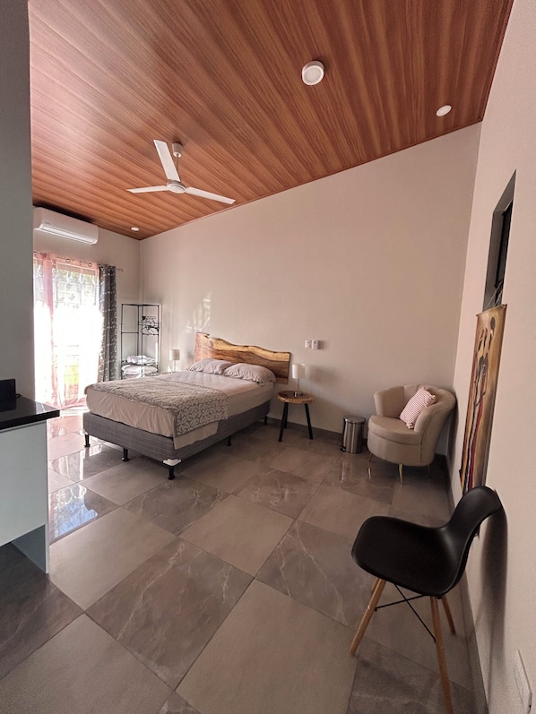 A modern bedroom with a bed, a chair, a small table, and a ceiling fan.