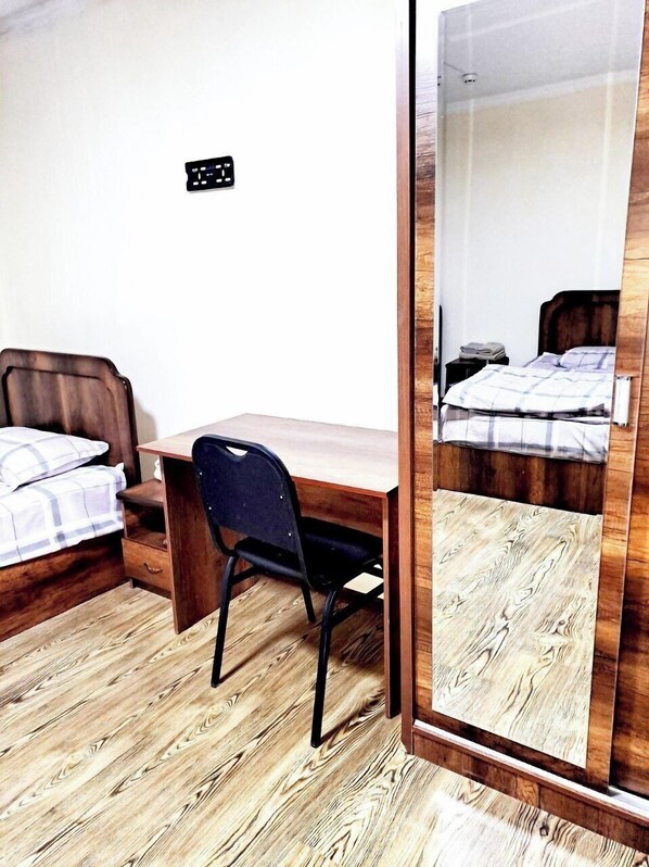 A bedroom with a wooden desk, a chair, a bed with a plaid blanket, a mirror, and a wooden floor. - Hotel Mir (Bukhara)