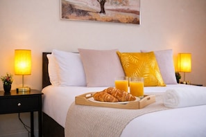 Een netjes opgemaakt bed met een dienblad croissants en sinaasappelsap, twee bedlampen en een schilderij aan de muur.