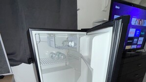 Ein Zimmer mit Kühlschrank, Fernseher mit Roku-Oberfläche und Fliesenboden.