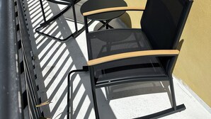 Un balcone con due sedie, un tavolino, un muro giallo e una ringhiera in metallo.