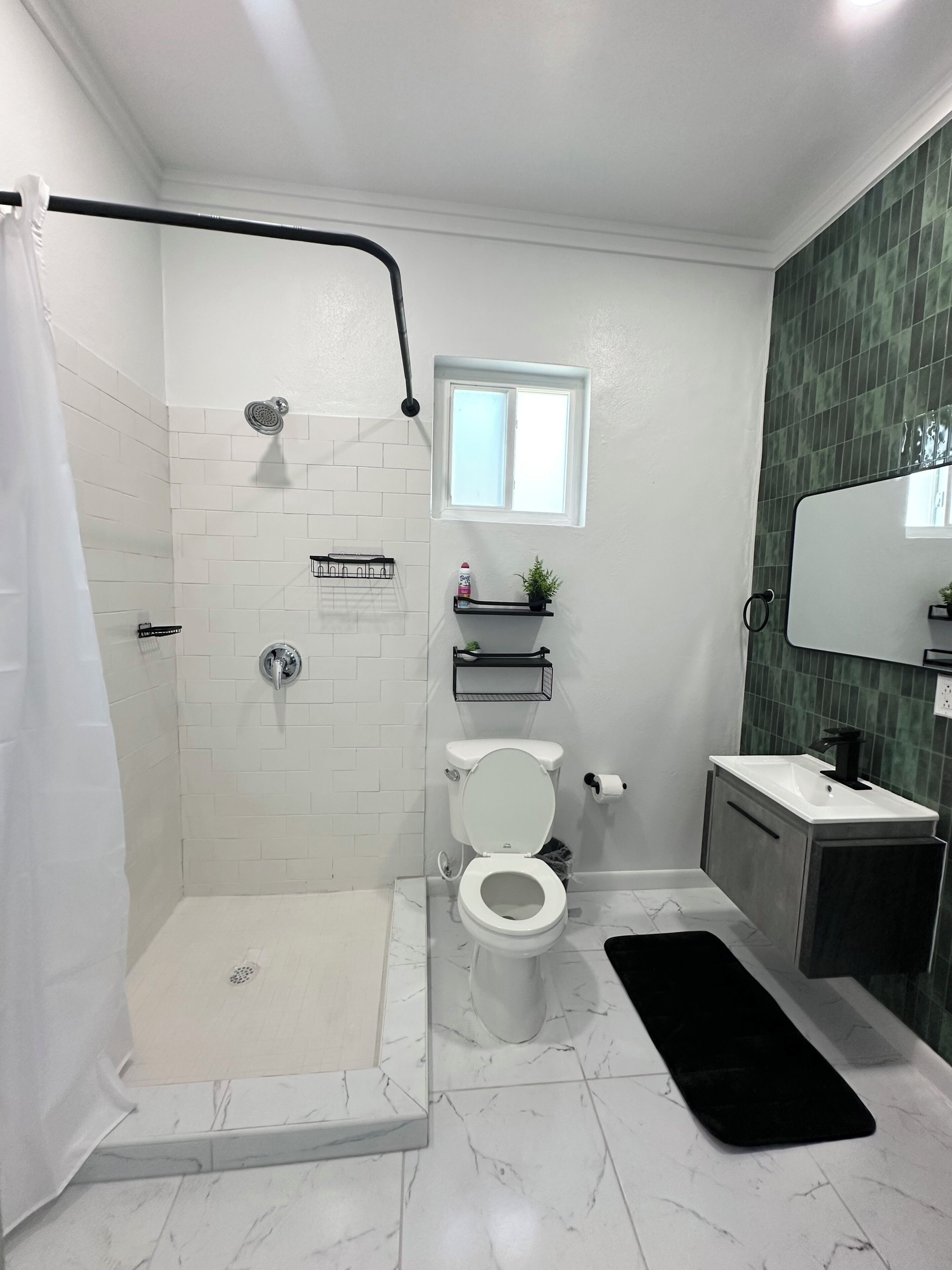 Un baño con ducha, inodoro, lavamanos y un pequeño ventanal.