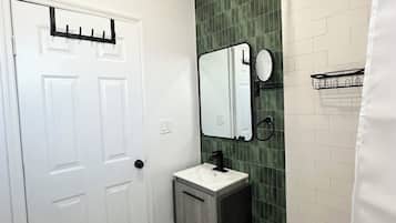 Un bany amb una porta blanca, un lavabo amb aixeta negra, un mirall i un teló de bany.
