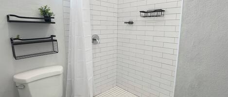 A bathroom with a white toilet, a shower with a white tiled wall, a black shower curtain, and a black rug.