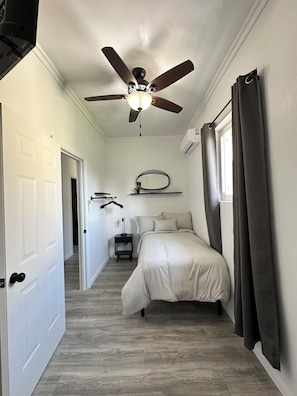 A bedroom with a ceiling fan, a bed, a nightstand, a mirror, and a window with curtains.