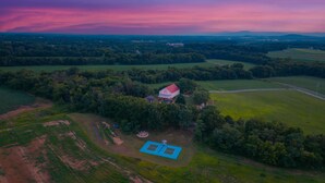 An aerial view of a rural property with a large barn, a tennis court, and surrounding fields. - The Farm Apartment at Gettysburg Farmstead (Mount Joy Township)