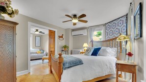 A bedroom with a bed, wooden furniture, a ceiling fan, an air conditioning unit, and a window with curtains. - The Farm Apartment at Gettysburg Farmstead (Mount Joy Township)