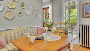A dining area with a wooden table, a white doily, a vase with flowers, and a striped sofa. - The Farm Apartment at Gettysburg Farmstead (Mount Joy Township)