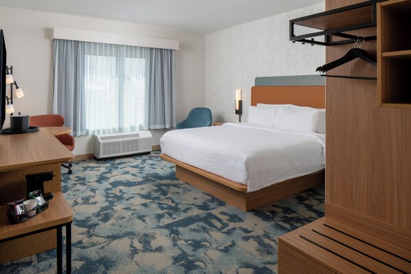 Ett hotellrum med en säng, ett skrivbord, en stol, ett element och ett fönster med gardiner.