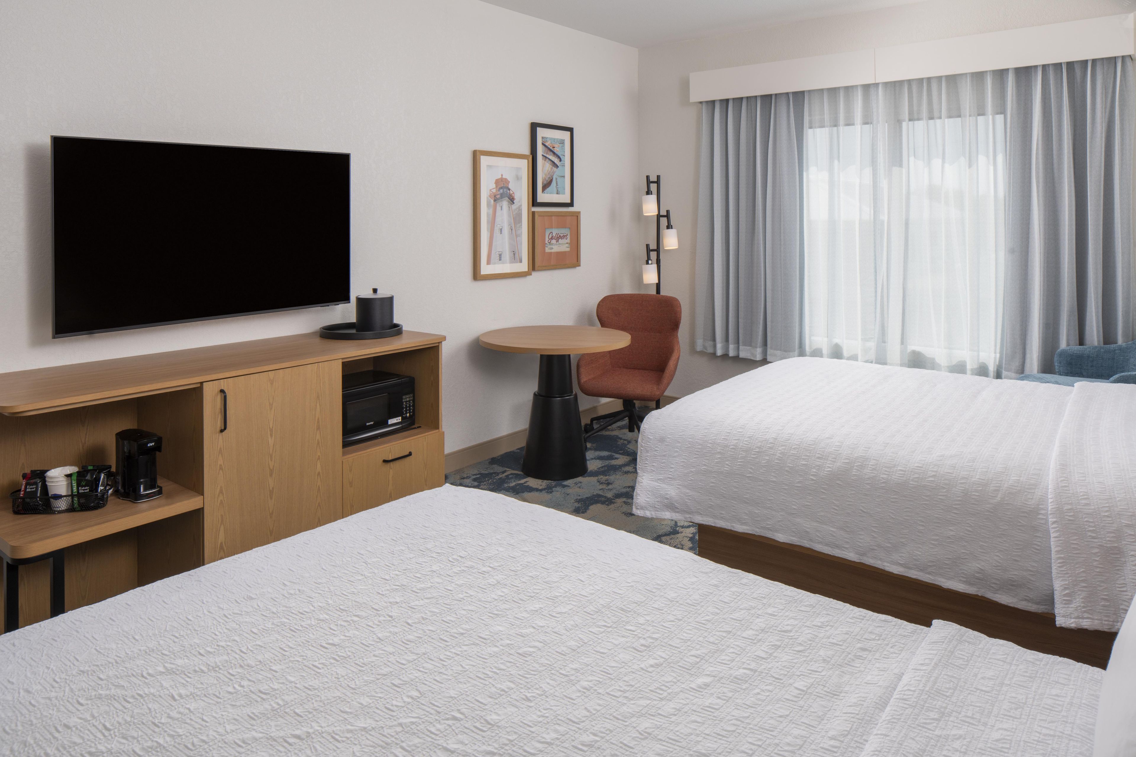 A hotel room with two beds, a flat-screen TV, a coffee maker, a small table, and a chair.