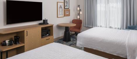 A hotel room with two beds, a flat-screen TV, a coffee maker, a small table, and a chair.
