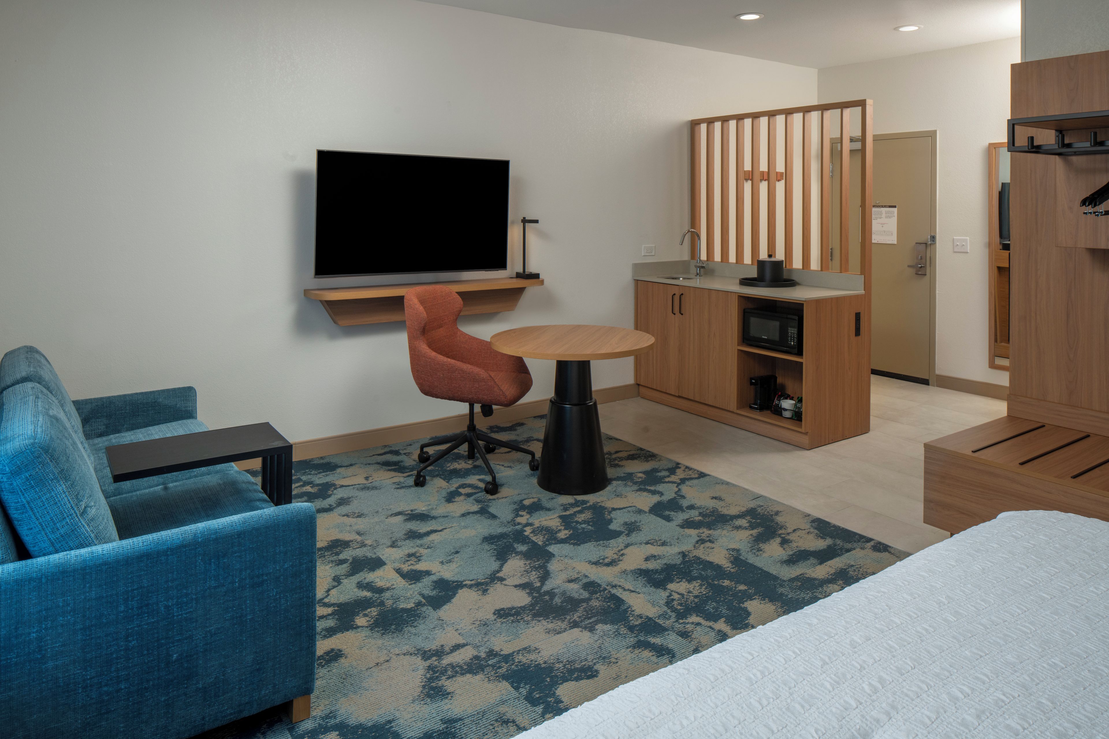 Een hotelkamer met een bed, een blauwe fauteuil, een klein rond tafeltje, een televisie, een kitchenette en een kledingkast.