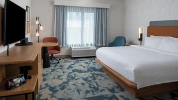 Habitación de hotel con cama, escritorio, silla, televisor y ventana con cortinas.