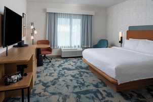 Habitación de hotel con cama, escritorio, silla, televisor y ventana con cortinas.