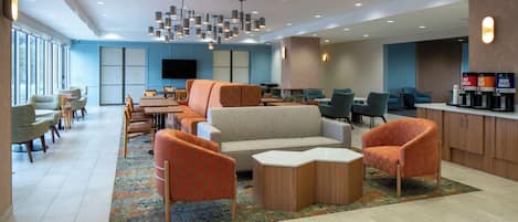 Un hall d’hôtel moderne doté d’espaces de détente, d’un téléviseur à écran plat et d’un coin café.