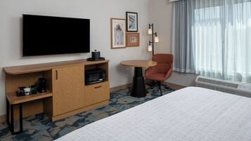 A hotel room with a bed, a TV, a desk with a microwave, a chair, and a window with curtains.