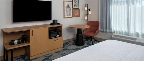 Habitación de hotel con cama, televisión, escritorio con microondas, silla y ventana con cortinas.
