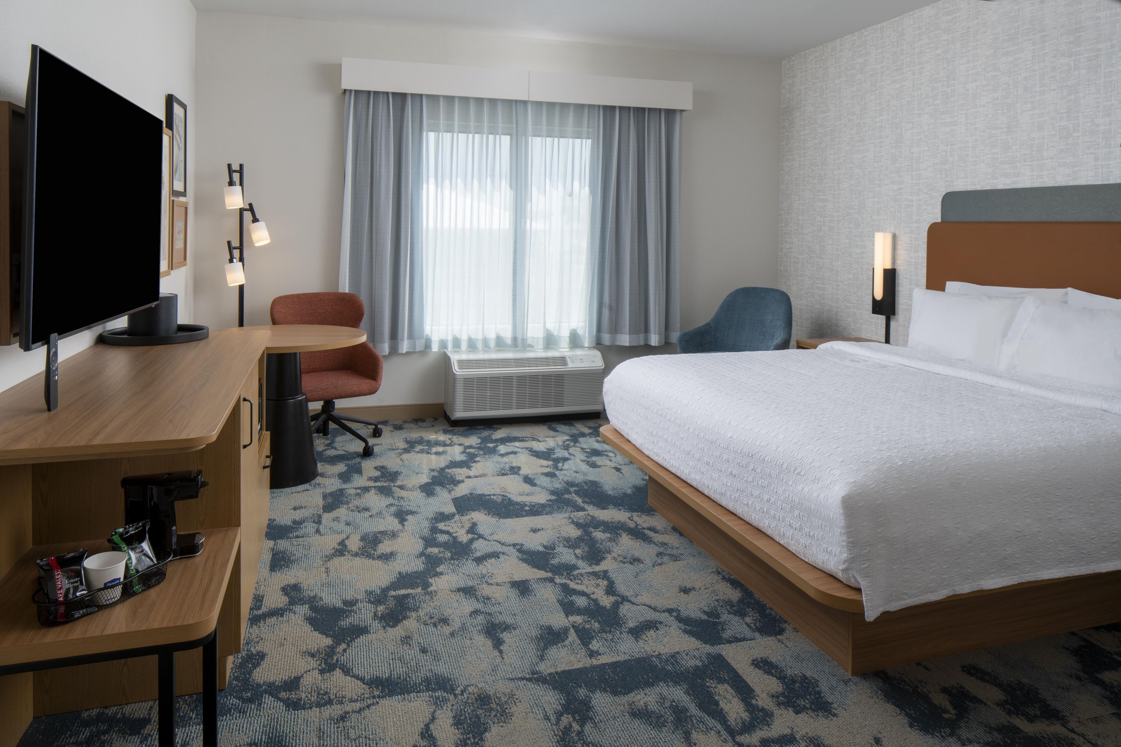 A hotel room with a bed, a desk, a chair, a television, and a window with curtains.