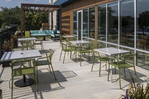 Un espace extérieur aménagé en terrasse, avec des tables et des chaises, un canapé et une pergola illuminée de guirlandes lumineuses.