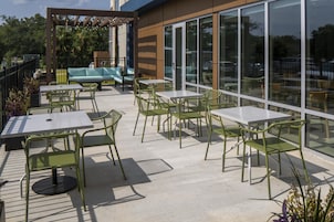 Un espacio de patio al aire libre con mesas y sillas, un sofá y una pérgola con luces colgantes.
