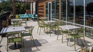 Ulkoterassi, jossa on pöytiä ja tuoleja, sohva sekä köynnöskasveilla koristeltu pergola, johon on ripustettu valonauhoja.
