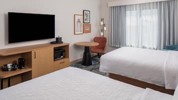 Habitación de hotel con televisión de pantalla plana, cafetera, una mesita, una silla y dos camas.