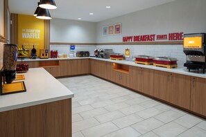 Een moderne keukenruimte met een pannenkoekenstation, een sapautomaat en een bord met ontbijtproducten.