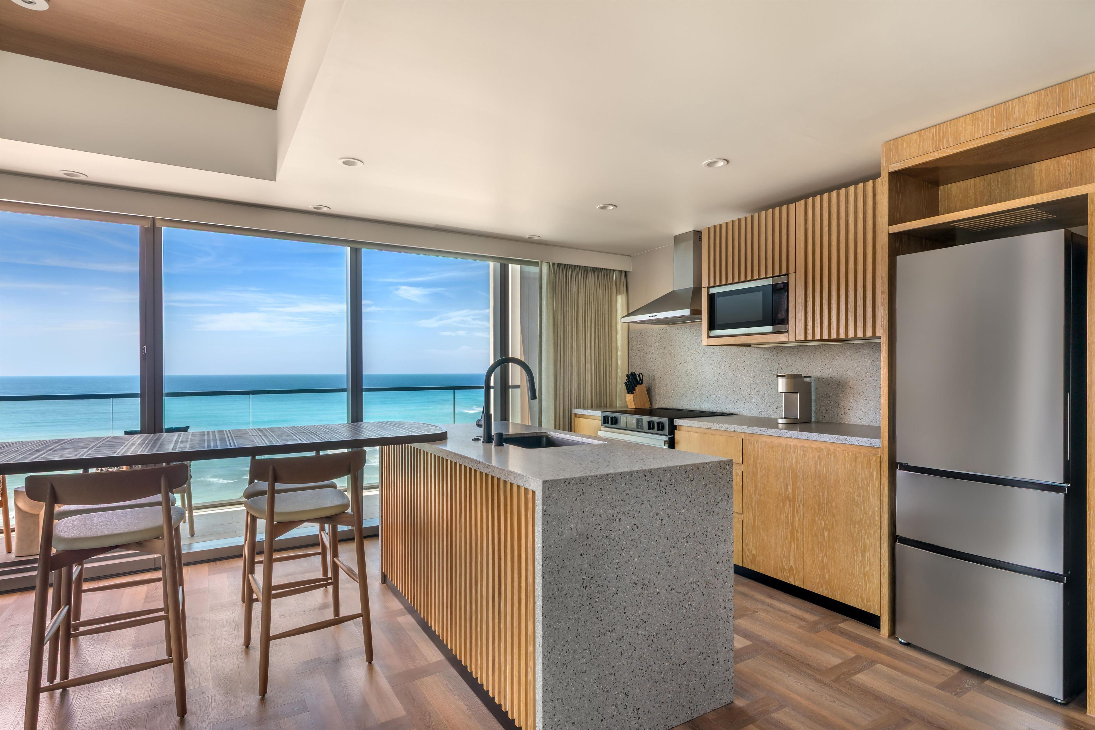 A modern kitchen with a large island, wooden cabinets, and a view of the ocean.