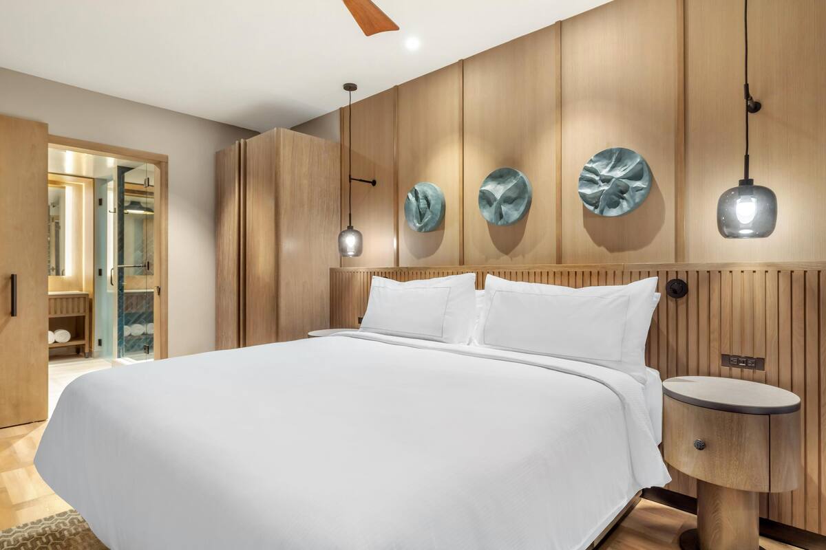 Een moderne slaapkamer met een groot bed, houten lambrisering en hanglampen.